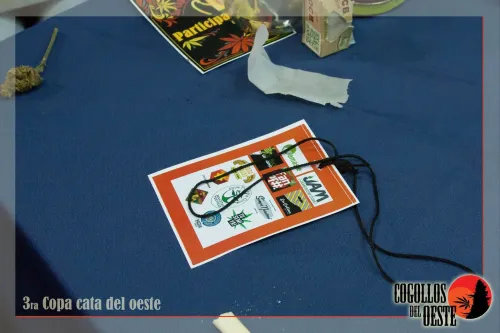Credencial con logos de marcas sobre el mantel, junto a papelillos y una flor, Copa Cata del Oeste 2016