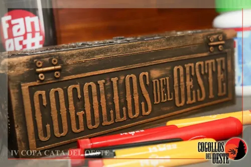 Caja de madera tallada con el nombre de la asociación, junto a tubos de colores, Copa Cata del Oeste 2017