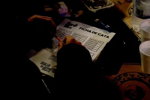 Manos completan una ficha de cata en penumbra, junto a vasos y un encendedor, Copa Cata del Oeste 2019