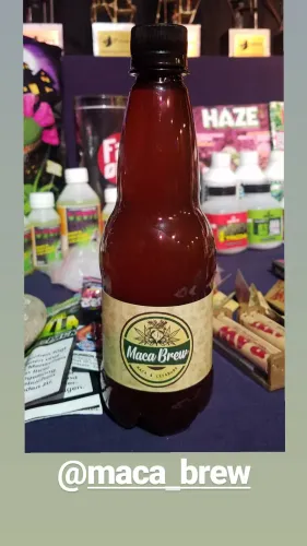 Botella de una bebida de maca frente a productos de cultivo, papelillos y los trofeos, Copa Cata del Oeste 2019