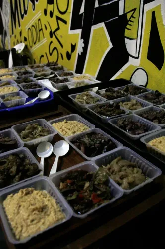 Bandejas descartables con comidas frías y cucharas de servir, ante un mural pintado, Copa Cata del Oeste 2019