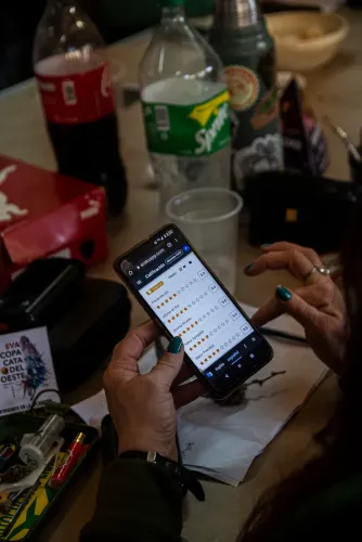 Manos califican una muestra en la aplicación del celular, junto a una credencial, Copa Cata del Oeste 2022