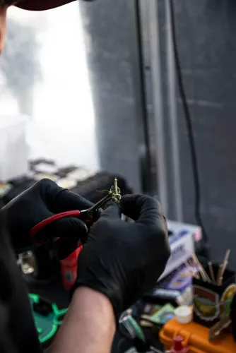 Manos con guantes negros recortan un cogollo con una tijera roja en un stand, Copa Cata del Oeste 2022