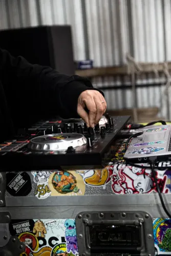 Una mano maneja el controlador de DJ sobre una valija de equipos cubierta de stickers, Copa Cata del Oeste 2022