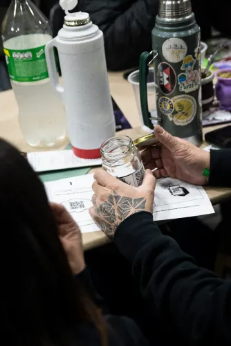 Una mano tatuada sostiene un frasco de muestra con código QR junto al instructivo, Copa Cata del Oeste 2022