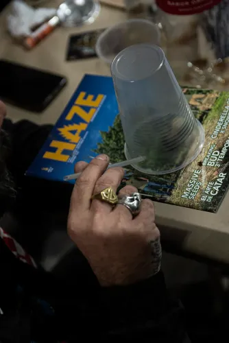 Una mano con anillos sostiene una pajita bajo un vaso invertido sobre una revista, Copa Cata del Oeste 2022