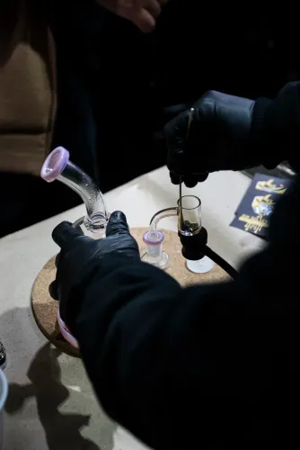 Manos con guantes negros cargan extracto con una herramienta en una pipa de vidrio, Copa Cata del Oeste 2022