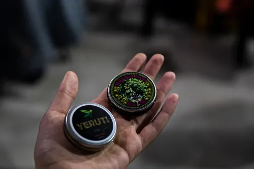 Una mano abierta muestra dos latas con los logos de marcas cannábicas, Copa Cata del Oeste 2022
