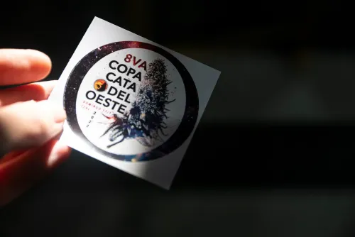 Una mano sostiene el calco redondo de la edición con el logo y la fecha, Copa Cata del Oeste 2022