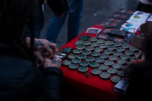 Manos tatuadas arman un porro frente a un stand con latas sobre un mantel rojo, Copa Cata del Oeste 2022